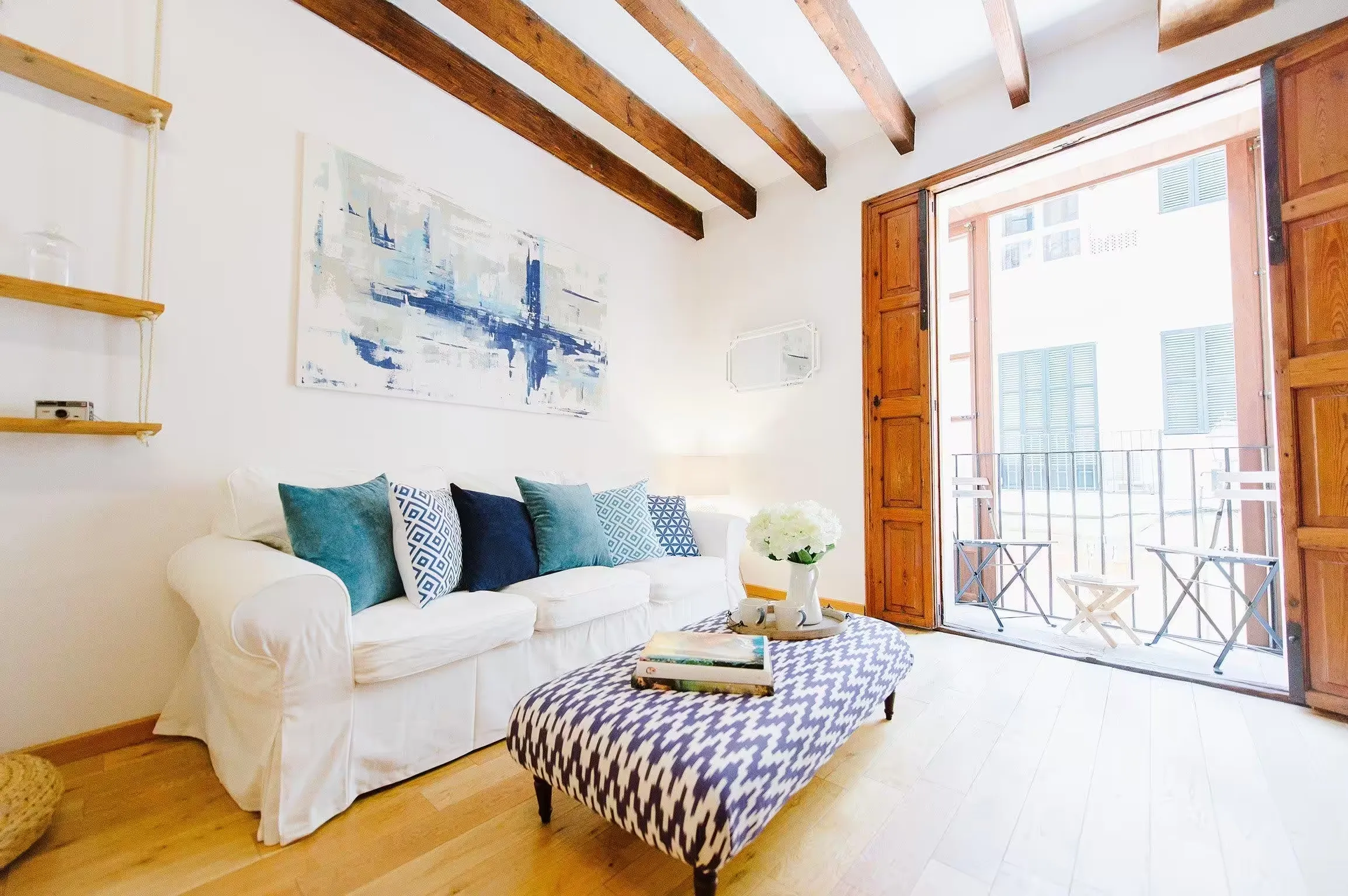 Sitting room at Casa Roca in Palma with timber ceiling beams, a white sofa and tall shutters open onto a balcony