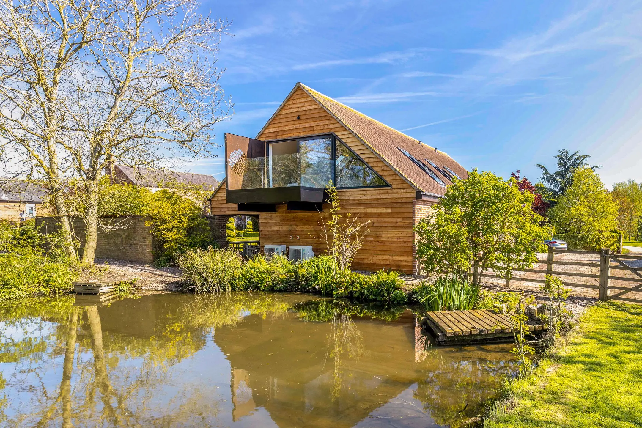 The Loft at Clipston, a timber-clad stable conversion with a glass balcony overlooking the estate pond