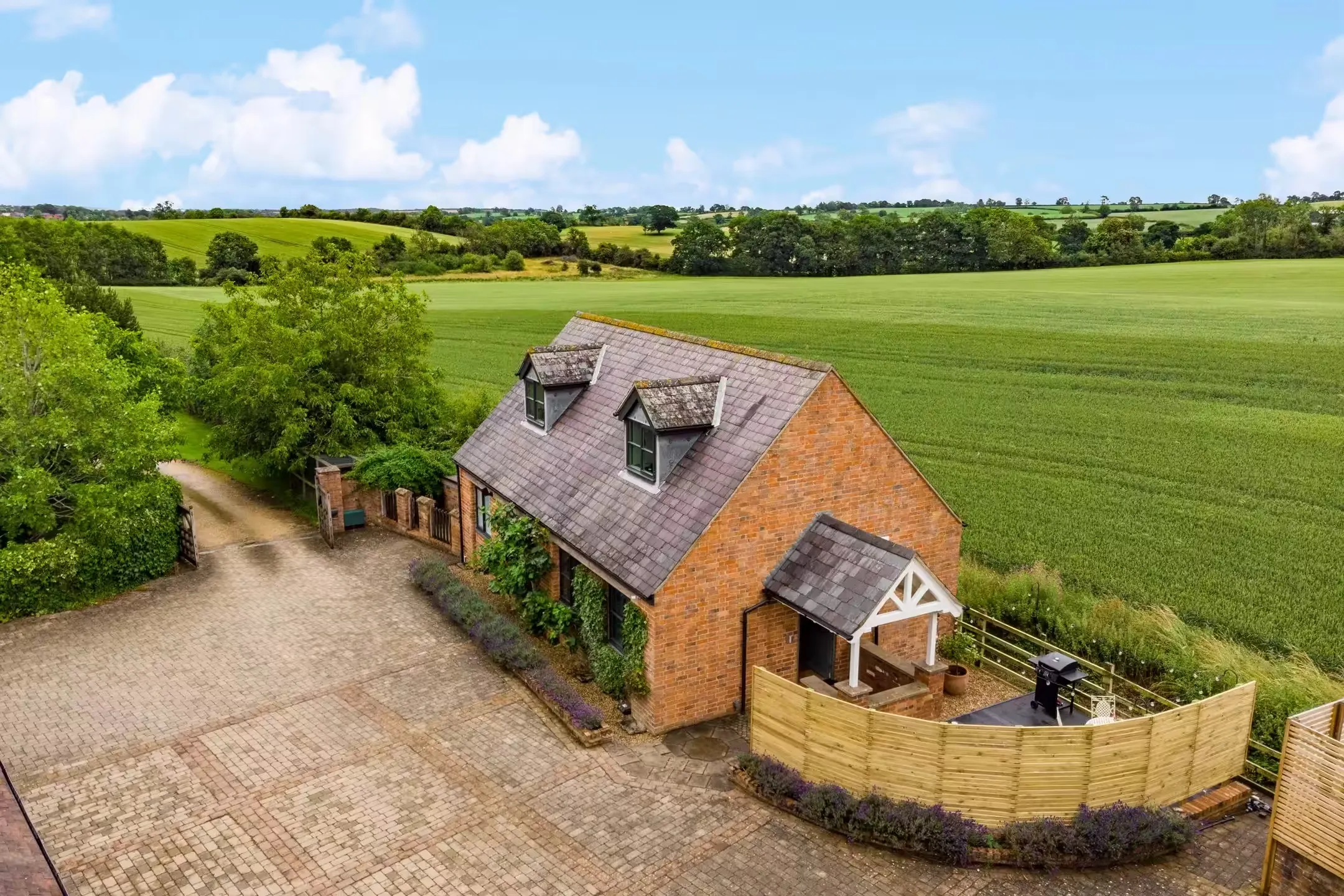 Aerial view of The Cottage, a red-brick former dovecote surrounded by fields at Clipston