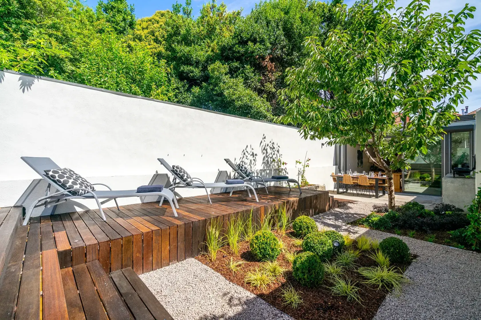 Walled garden at Villa Almada in Porto with a timber sundeck, sun loungers and a shaded dining terrace