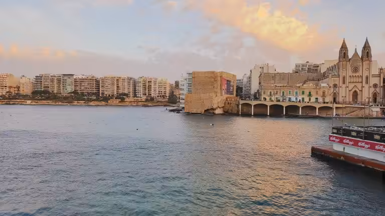 Balluta Bay in Malta at sunset with the twin-spired Carmelite church and the Sliema apartment blocks beyond