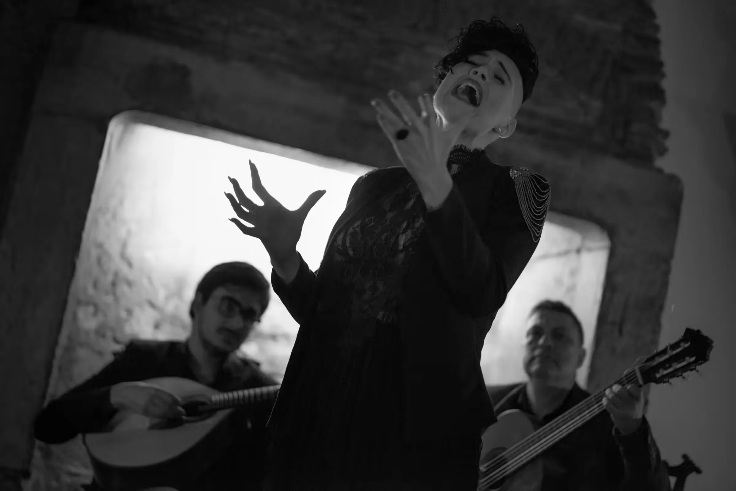 Fadista singing in a black shawl with a guitarra portuguesa player and a viola player behind her