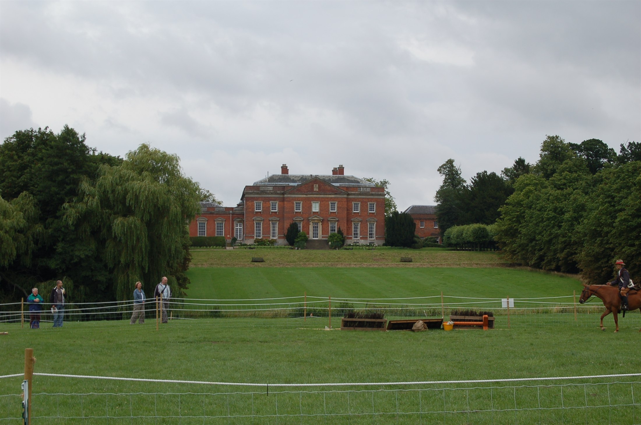 The red-brick Palladian front of Kelmarsh Hall in Northamptonshire across parkland with cross-country fences