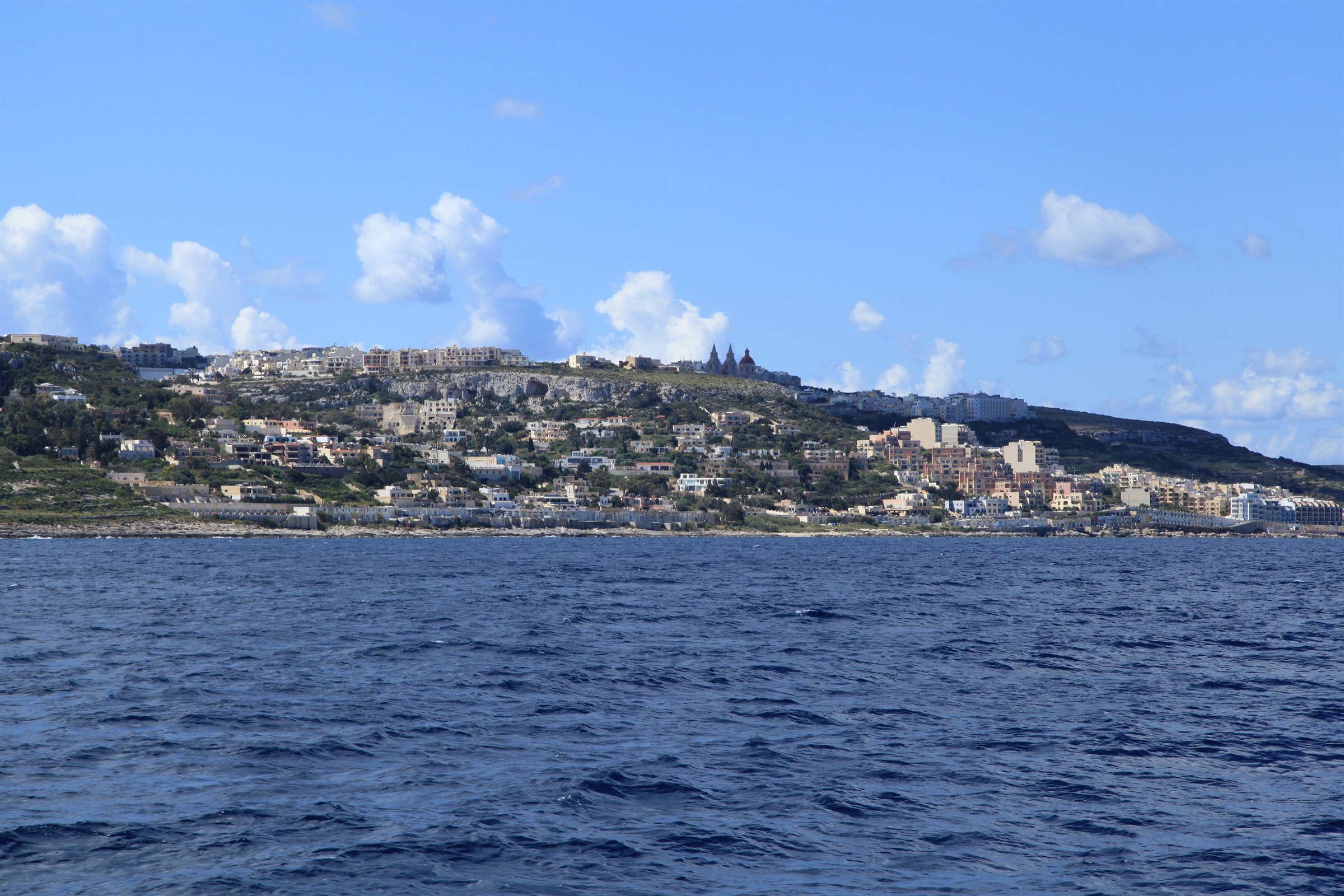 The town of Mellieha on its ridge in northern Malta seen from the sea with the parish church domes on the skyline