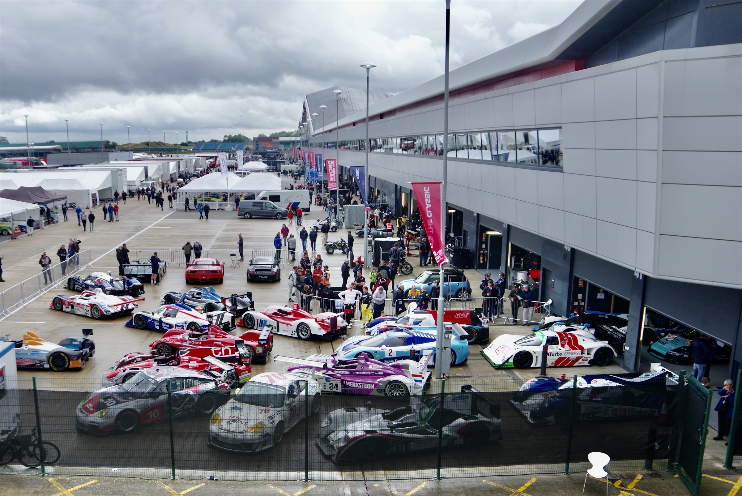 Rows of endurance prototypes and GT racing cars parked in the Silverstone paddock in front of the Wing