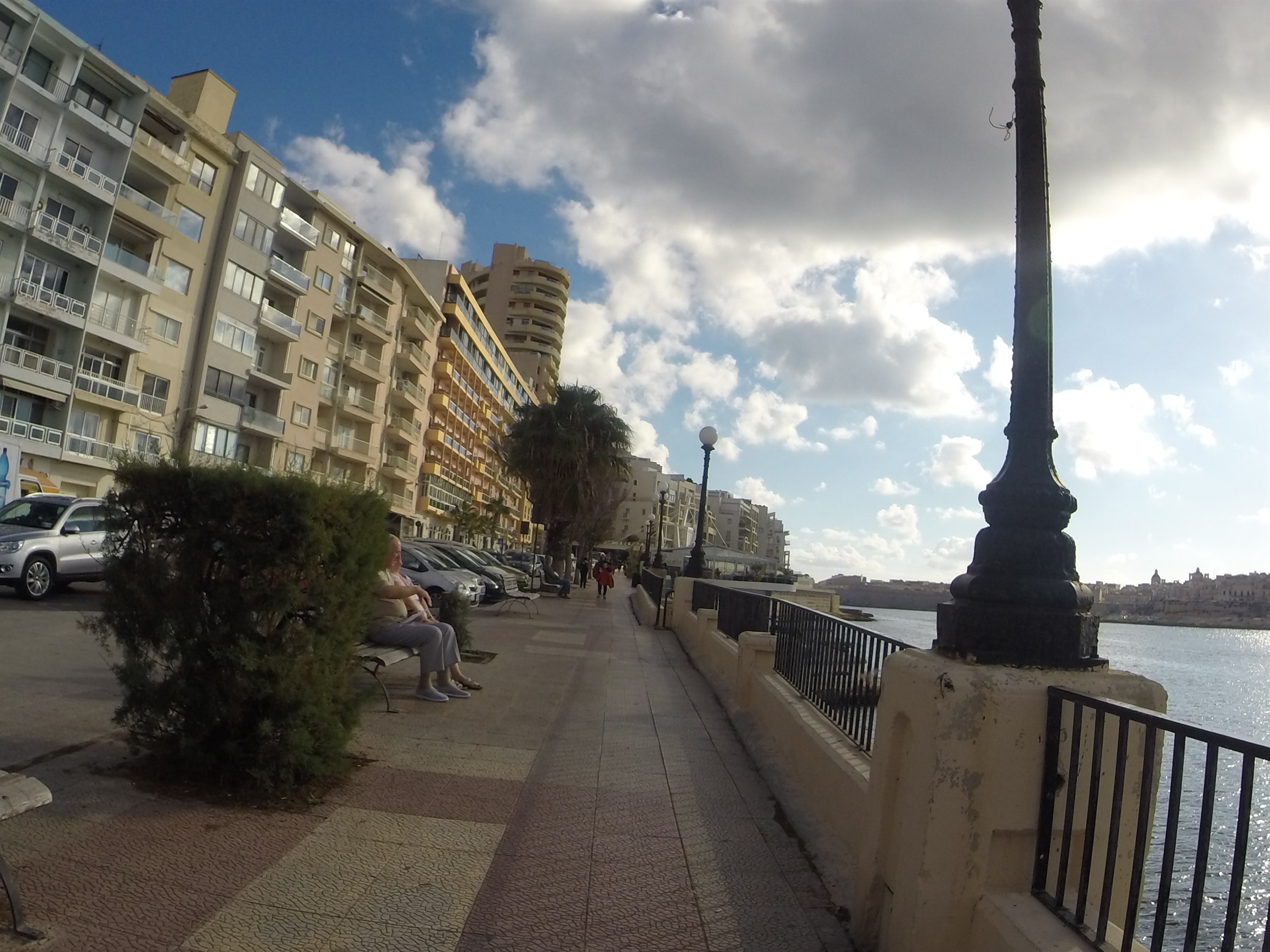 The Sliema seafront promenade in Malta with apartment blocks, palm trees and Valletta on the horizon