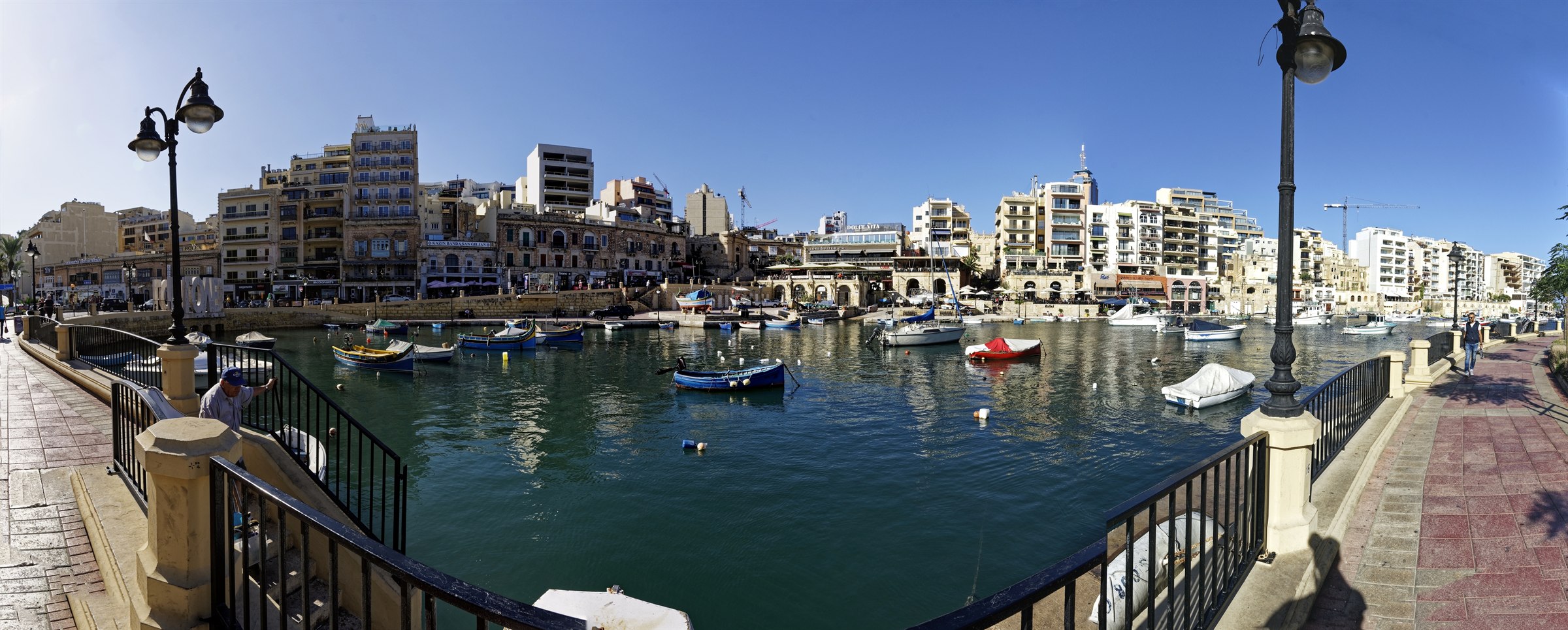 Spinola Bay in St Julians Malta with traditional luzzu fishing boats moored in front of waterfront restaurants