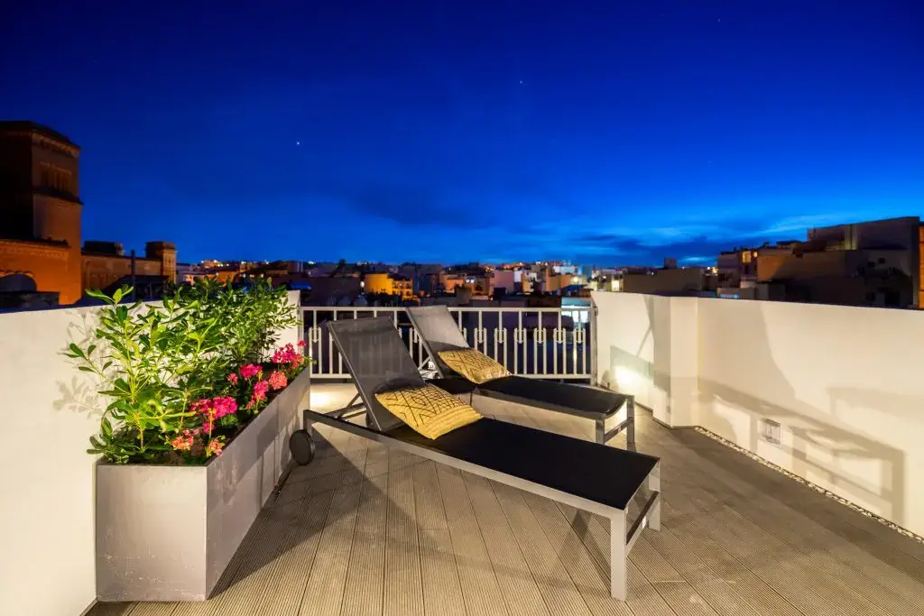Rooftop terrace at Aster House in Sliema at dusk with two sun loungers and the lit rooftops of Sliema beyond