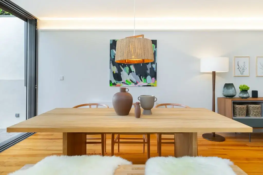Solid oak dining table under a woven pendant light at Villa Almada in Porto, with original artwork on the wall behind