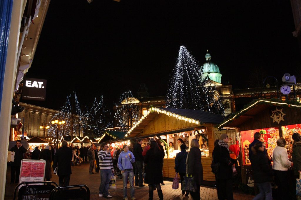Wooden chalets of the Frankfurt Christmas Market in Victoria Square, Birmingham, lit at night with the Council House dome behind