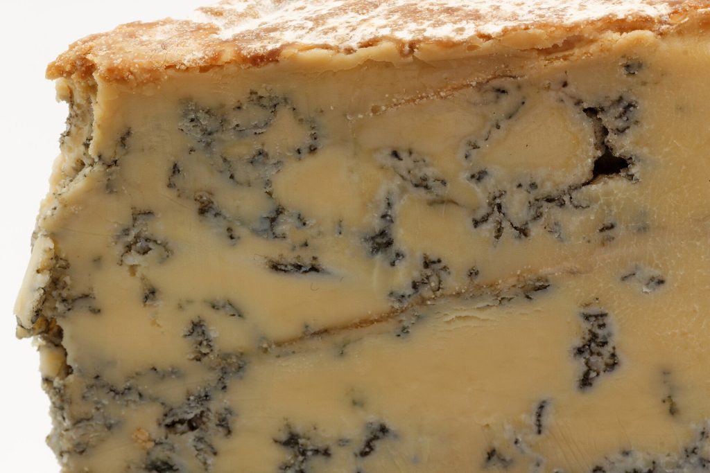 Close-up of a wedge of Blue Stilton cheese showing its creamy paste, blue veins and crusty rind
