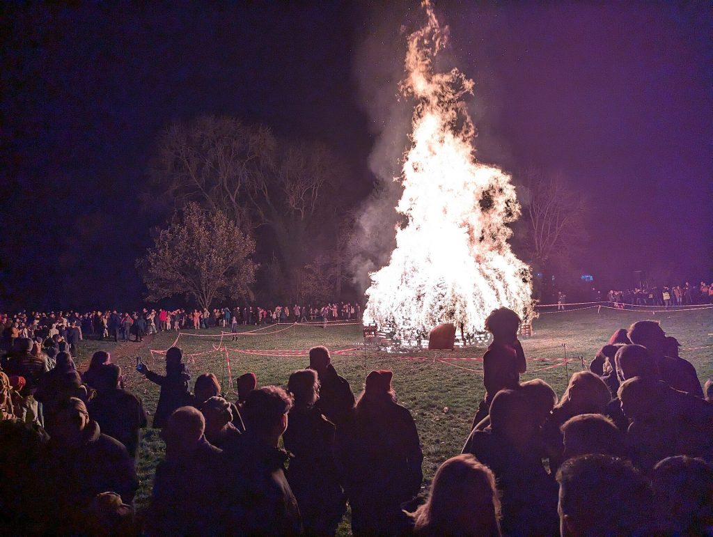 Crowds gathered around a large community bonfire on Bonfire Night in an English village field