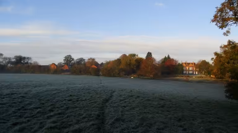 Frost on a field path near Welford, Northamptonshire, with autumn trees and a red-brick house in early morning light