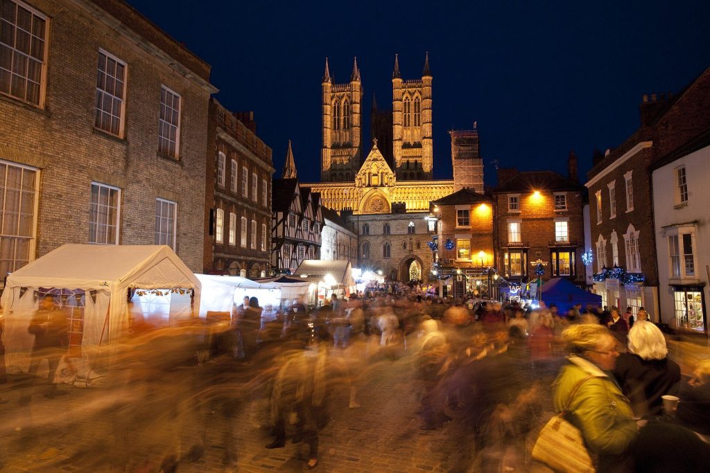 Crowds and market stalls on the cobbled approach to the floodlit west front of Lincoln Cathedral at Christmas