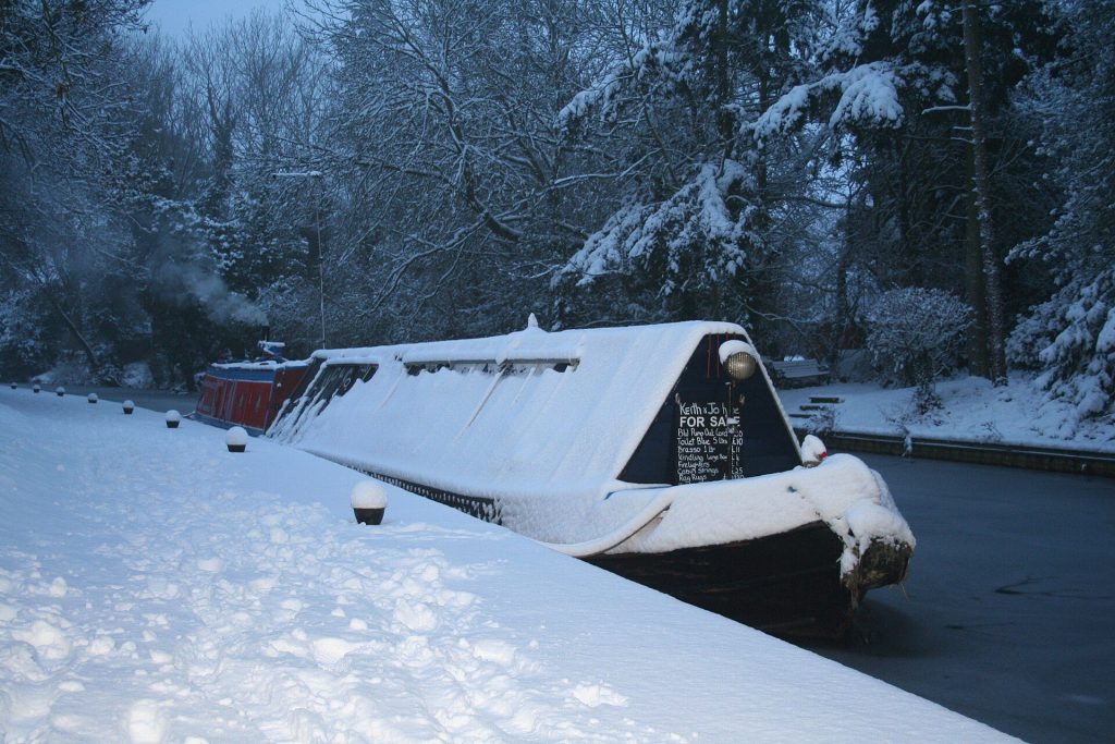 A snow-covered narrowboat moored on the frozen canal at Market Harborough with snowy trees along the towpath