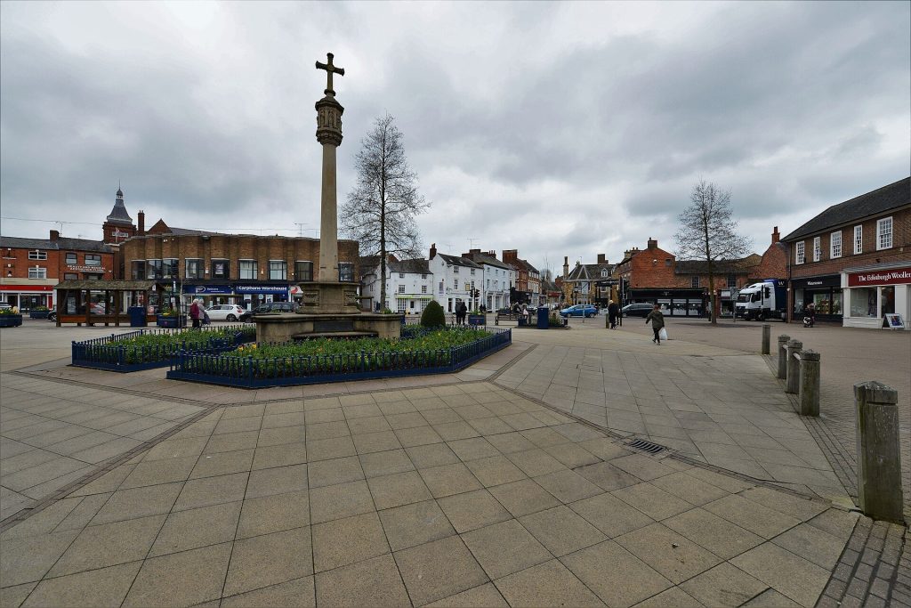 The Square in Market Harborough town centre with its stone memorial cross, shops and old buildings