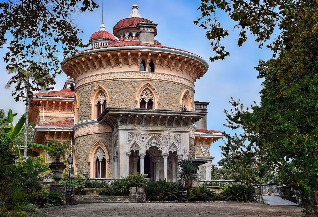 The round stone tower, carved arches and red domes of Monserrate Palace in Sintra framed by trees
