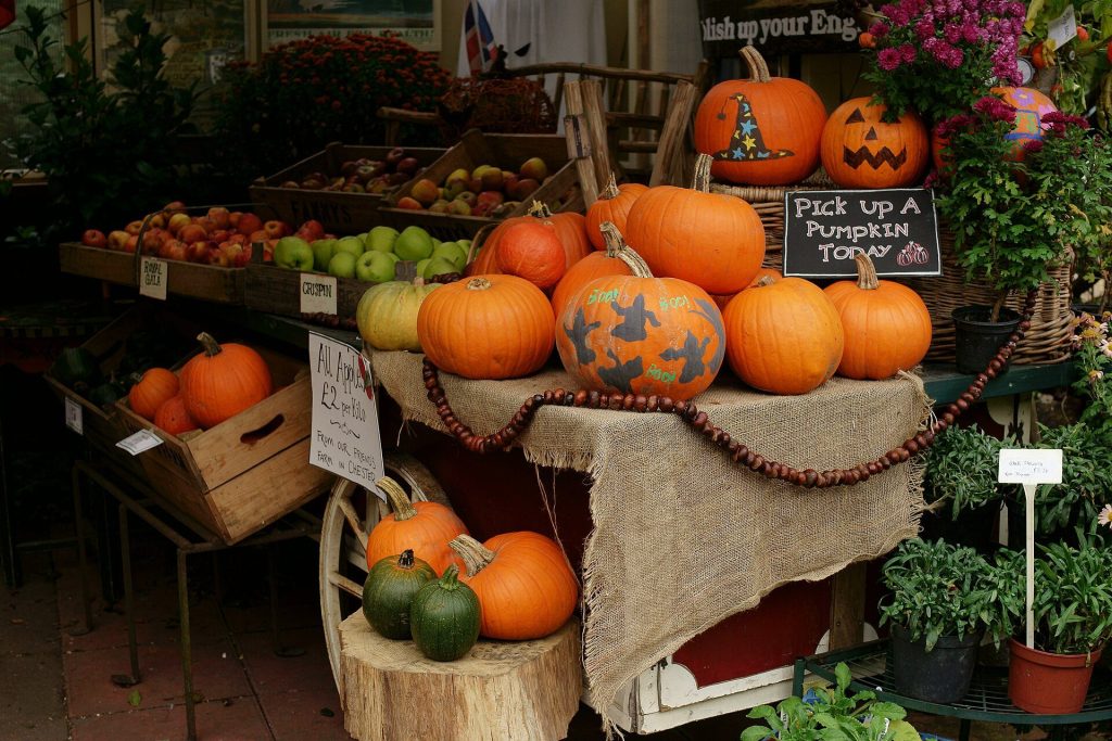 Pumpkins and squashes piled on a cart outside an English farm shop with crates of apples and a pick up a pumpkin sign