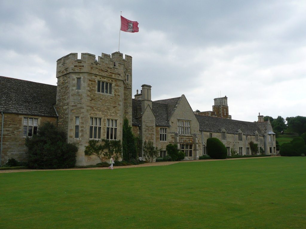 The stone front of Rockingham Castle with its crenellated tower, red flag and lawn