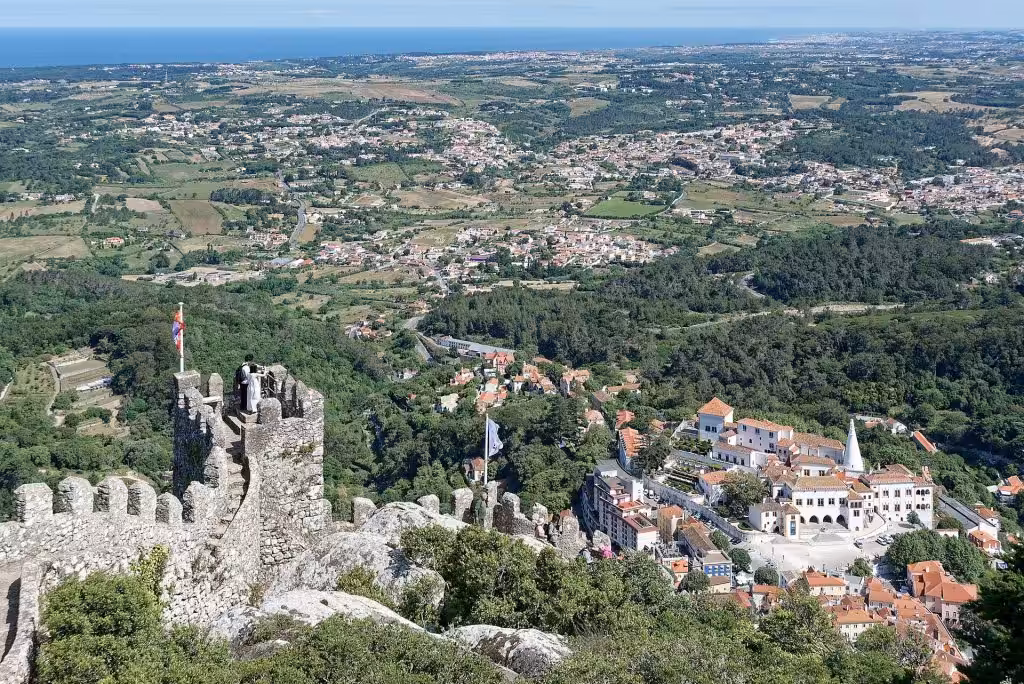 The walls of the Moorish Castle in Sintra looking down on the town and the white Sintra National Palace with the Atlantic beyond