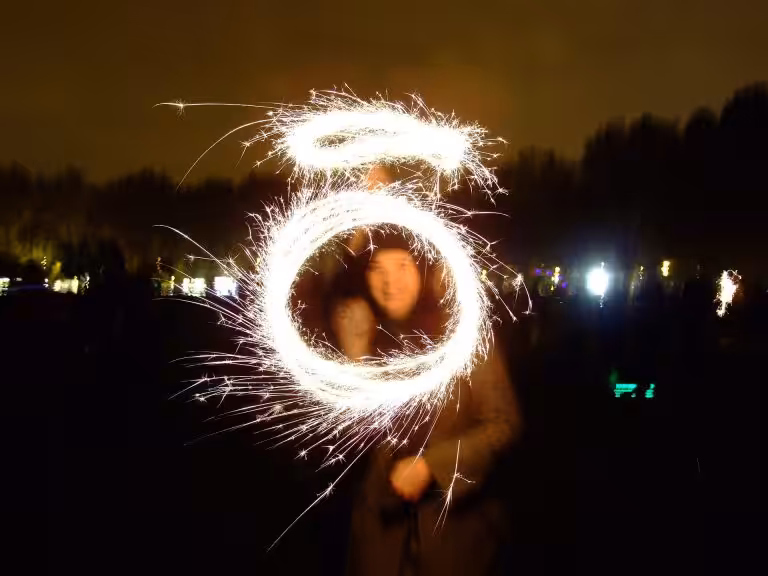 A sparkler traced into glowing circles around a smiling woman on Bonfire Night