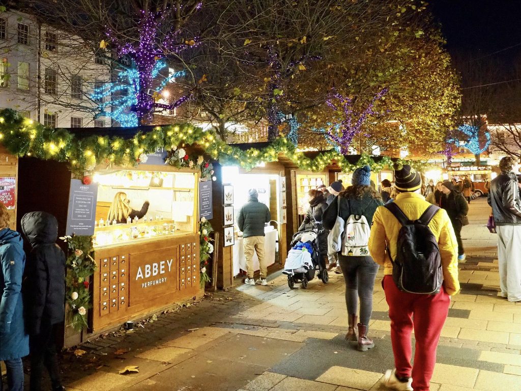 Garland-trimmed chalets and shoppers at York Christmas Market on Parliament Street with lights in the trees